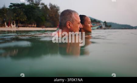 Diverse couple enjoying tropical sunset swim, embracing love and relaxation Stock Photo