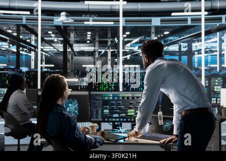 Server room manager supervises engineer working with AI visual programming to improve gear. Stock Photo