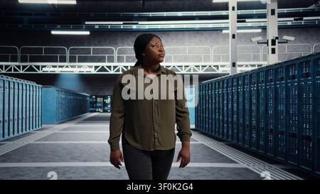 IT administrator walking through server facility rows of servers, rolling out advanced cooling and power management solutions. IT specialist supervising server facility, reducing energy consumption. Stock Photo
