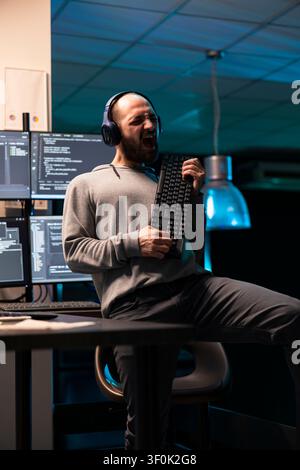 Adult software developer pretends to play keyboard instrument while listening to music during break. The humorous scene captures creativity and stress relief in modern programming environment. Stock Photo