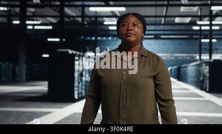 Software engineer walking in server facility, checking hardware for system stability. IT administrator supervising server environment room, checking infrastructure systems. Stock Photo