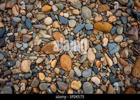 A full frame, top-down view of smooth, colorful river pebbles and sand. A natural, earthy texture background with various shades of brown, gray, blue, Stock Photo