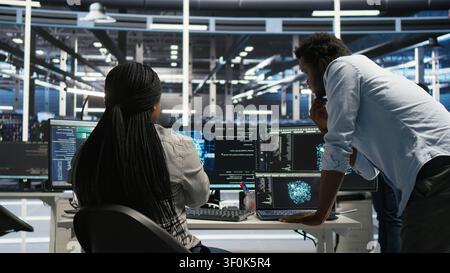 Server facility supervisor supervising staff member rolling out AI solutions optimizing equipment. Server environment supervisor supervising coder applying AI to minimize systems downtime. Stock Photo