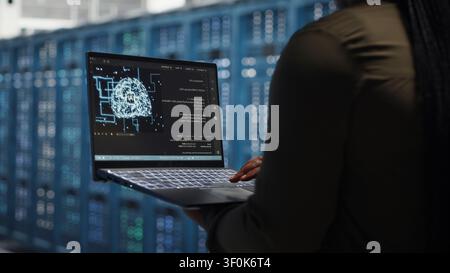 Data center engineer uses a laptop in a server room to upgrade server rigs and increase workload capacity. Stock Photo