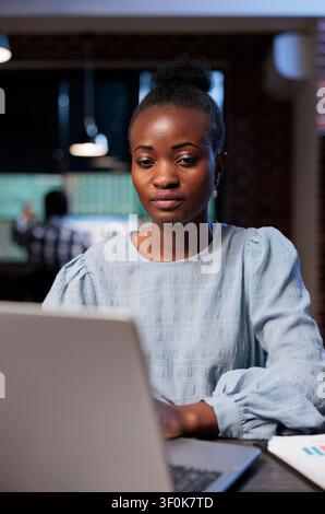 Confident African American woman uses a laptop for real time market analysis, reviewing forex statistics in an agency workspace, showing financial research, trading risk and investment decision. Stock Photo