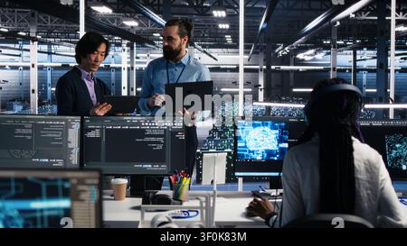 High tech server room team supervisor supervising work done by programmers working on neural network software, while supervisor overseeing IT staff members implementing deep learning tech. Stock Photo