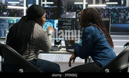Server facility coworkers discussing ideas, applying AI ML models to set up equipment. IT experts cooperating in server environment, working on optimizing systems. Stock Photo