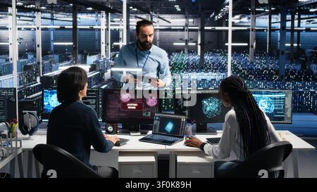 High tech server room team supervisor coordinating programmers repairing urgent system alert. Stock Photo