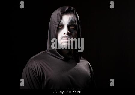 Young man looks serious at the camera while dressed as a grim reaper, creating a dark Halloween costume portrait over a black background. Stock Photo