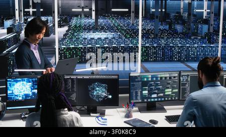Software developers collaborating in computing facility, checking AI diagnostics on computer, while IT staff members discussing in server room, enhancing machine learning systems. Stock Photo