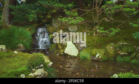 Kanazawa, Japan - Oct 6 2024, panoramic view of a small waterfall and stream among the trees in Kenroku-en Park, without people, at daytime, Kanazawa, Stock Photo