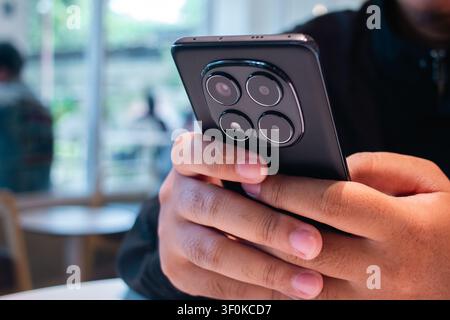 A detailed close up image showing a person hands holding a mobile device in a modern cafe setting with a blurred background of patrons enjoying their Stock Photo