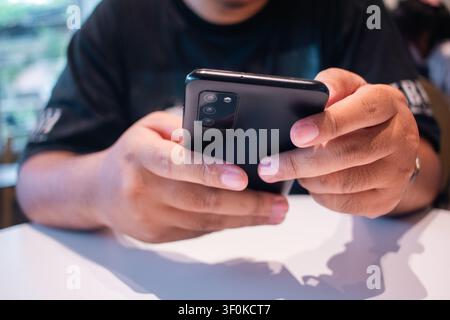 Close up depiction of a person focused on their mobile device while seated in a softly lit indoor environment showcasing casual style and engaging int Stock Photo