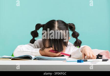 A tired young student hiding her face on the desk with books and stationery. Stock Photo