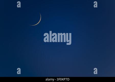 A beautiful thin crescent moon glowing in the clear deep blue evening sky, captured in Tamsui, New Taipei City, Taiwan. Stock Photo