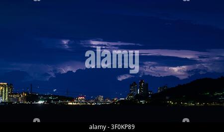 A dramatic night view of Tamsui, New Taipei City, featuring a powerful lightning storm illuminating the dark clouds above the illuminated urban skylin Stock Photo