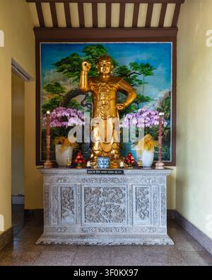 Golden Buddhist statue with fruit and orchid offerings on an ornate carved stone altar at Linh Ung Pagoda in Da Nang, Vietnam Stock Photo