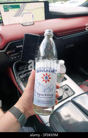 PLANO, TX, USA - JULY 06, 2026: A hand holds a Gerolsteiner sparkling water bottle inside a Mazda CX-70 vehicle with red leather interior. The vehicle Stock Photo