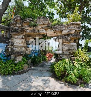 Natural stone archway entrance at Linh Ung Pagoda in Da Nang, Vietnam, featuring a paved path and lush tropical greenery in a peaceful garden setting Stock Photo