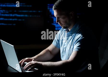 Hacker works on laptop with focus. Hacker analyzes encryption and security code. Hacker monitors digital network activity. Hacker performs hacking Stock Photo