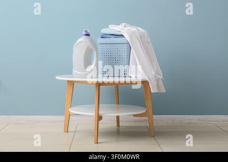 Laundry detergent bottle and basket with clean clothes on a modern side table against a blue wall, Set against a light blue wall, creating a clean and Stock Photo