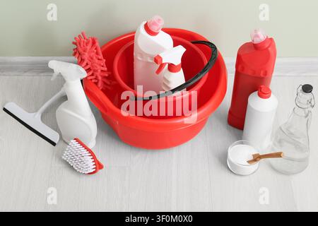 Cleaning supplies and tools including red buckets, spray bottles, and brushes on a light wooden floor Stock Photo