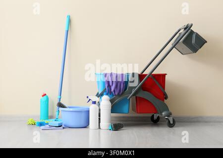 Professional cleaning supplies and equipment including a mop, bucket, and janitorial cart against a light wall Stock Photo
