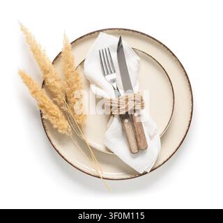Rustic table setting with ceramic plate, white napkin, cutlery, and dried pampas grass on a white background Stock Photo