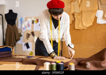 Young dark-haired woman in red hat working on fabric in a fashion design salon Stock Photo