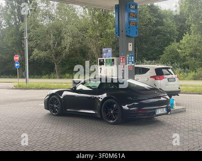 Cremona, Italy June 19th 2026 Black Porsche 911 Carrera S at a gas station pump, refueling next to illuminated digital fuel price displays Stock Photo