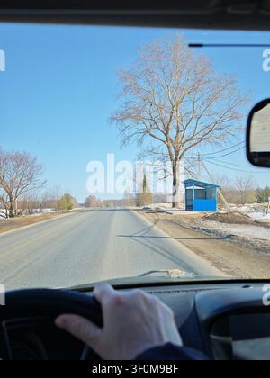 Driving along a road in spring, sunlight shines through the car window as trees and a bus stop pass by on the side. Stock Photo