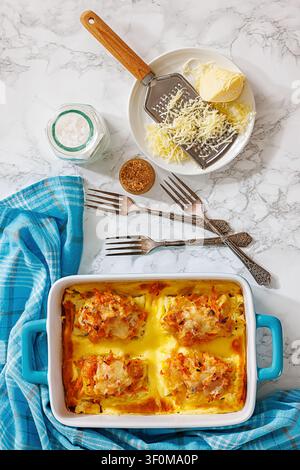 Ryba po grecku, Polish dish with white fish baked under carrots and onions in cheese sauce in a blue dish on marble table with forks and kitchen towel Stock Photo
