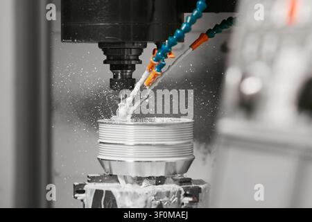 Milling machine drills holes on a metal part. CNC metalworking with coolant liquid. Industrial technologies concept. Stock Photo