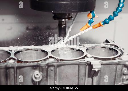 CNC milling machine grinds holes in car engine with coolant. Process of setting up engine cylinder blocks on a numerically controlled machine.  Stock Photo