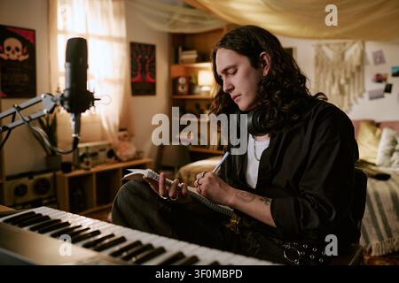 Long Haired Man Writing Song Lyrics in Home Music Studio for Content Marketing Stock Photo
