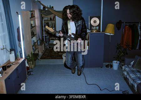 Man Jumping While Playing Electric Guitar at Home for Promotion Stock Photo