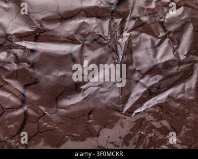 Background of transparent crumpled plastic bag filled with brown kinetic sand close-up Stock Photo