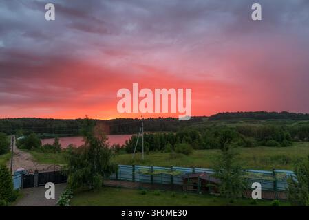 A sweeping elevated view over a Russian rural settlement reveals a small pond surrounded by mixed deciduous and coniferous forest. Stock Photo