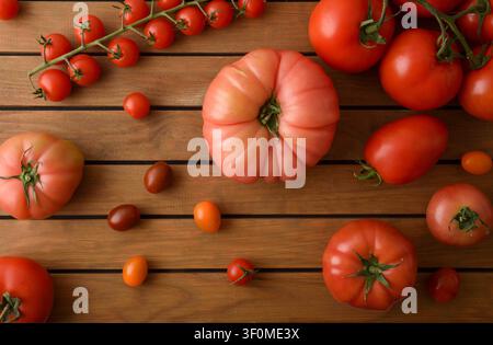 Top view of assorted fresh tomatoes on a rustic wooden table, featuring heirloom, cherry, roma, and vine varieties arranged with natural light and cop Stock Photo