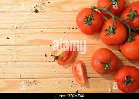 Fresh red tomatoes with two sliced pieces arranged on a rustic wooden surface. Bright natural light creates a clean composition with copy space for fo Stock Photo