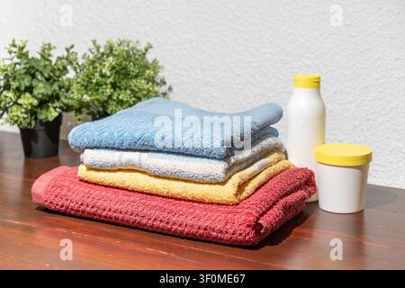 Stack of colorful folded towels with detergent containers placed on wooden table near potted plant Stock Photo
