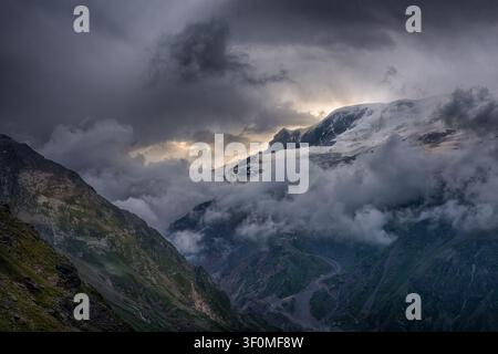A glaciated high-alpine peak rises above a deep mountain valley in the Greater Caucasus range. Stock Photo