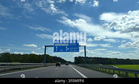 Road sign indicating directions to Berlin and Wismar along a highway with clear blue sky and green fields visible in the background Stock Photo