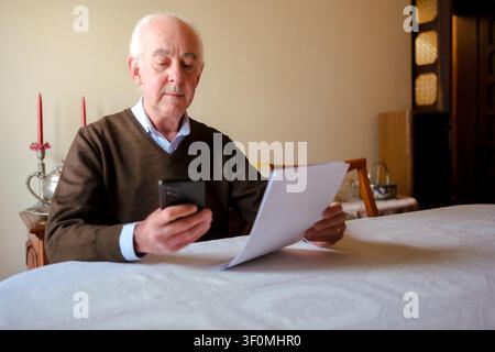 Senior man checking financial documents while using a mobile phone at home Stock Photo