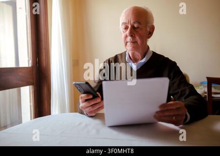 Senior man using smartphone while working with documents at a table Stock Photo