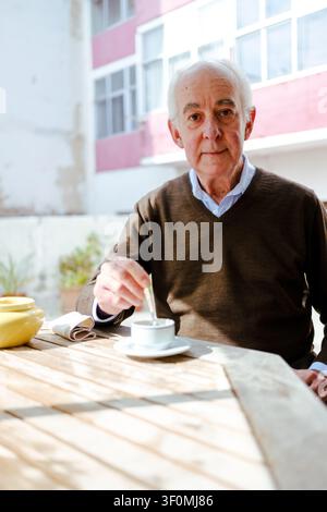 Elderly man stirring his tea, relaxing outdoors on a sunny day Stock Photo