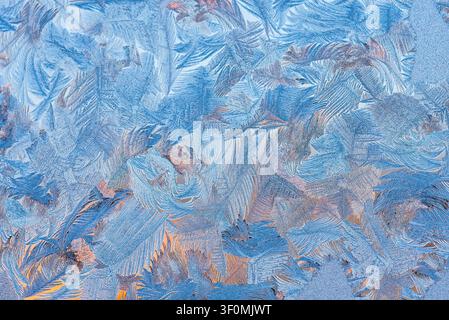 Extreme close-up macro photograph of intricate fern-like frost crystals formed on a glass windowpane. Stock Photo