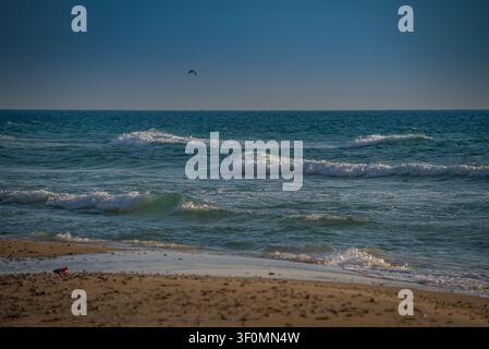 Rolling waves with white foam break onto a wide sandy beach along the Black Sea coast. Stock Photo