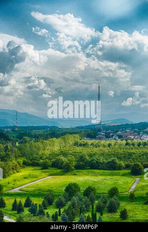 Elevated panoramic view over a lush green valley with a lattice television transmission tower rising above a scattered residential settlement. Stock Photo