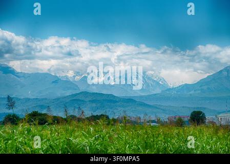 A sweeping panoramic view across a lush green foreground meadow toward a small lowland town. Stock Photo